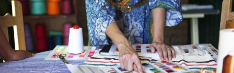 Independent business owner working in textile and crafts workshop. Woman wearing colourful peacock dress with colour palettes and threads. 