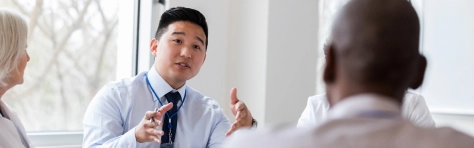 Professional group meeting with manager in an office setting. Asian man in smart wear / suit speaking to colleagues / employees about business processes.