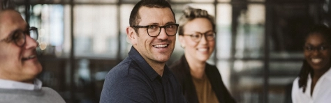 Mature man with glasses smiling in group meeting. Working together collaboratively with group in modern office. 