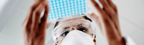 Image of a scientist with a mask and gloves on looking at a dish with samples in 