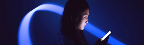 Business woman is looking at smartphone in a dark futuristic room with purple and blue lights. Digital world.