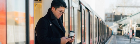 An image of a man stepping off the train whilst looking at his phone