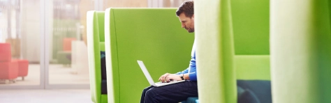 An image of a businessman with a laptop on his lap working in a an office 