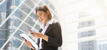 Woman looking at phone whilst holding laptop